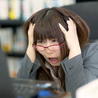 パソコンの前で頭を抱える赤い眼鏡の女性の写真