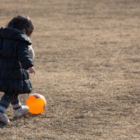 オレンジのボールを蹴る子どもの後ろ姿の写真