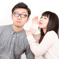 手を口元に当てて彼氏に内緒話をする黒髪の彼女の写真