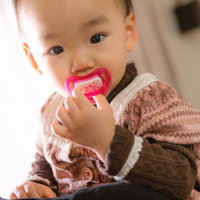 おしゃぶりを咥えて抱っこされる赤ちゃんの写真