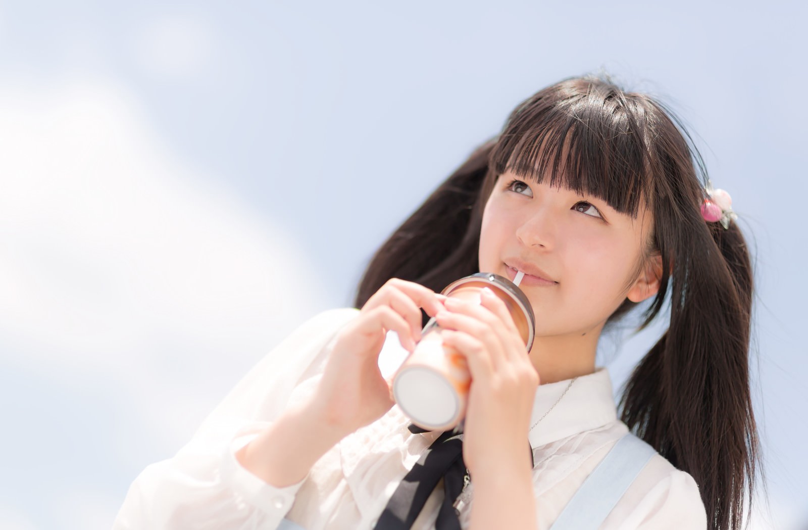 黒髪ツインテールの女の子が白いシャツで屋外でストローから飲み物を飲んでいる［モデル：こころ］