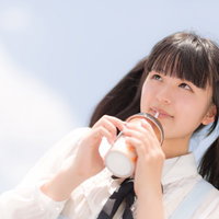 屋外でストローで飲み物を飲むツインテールの女の子の写真