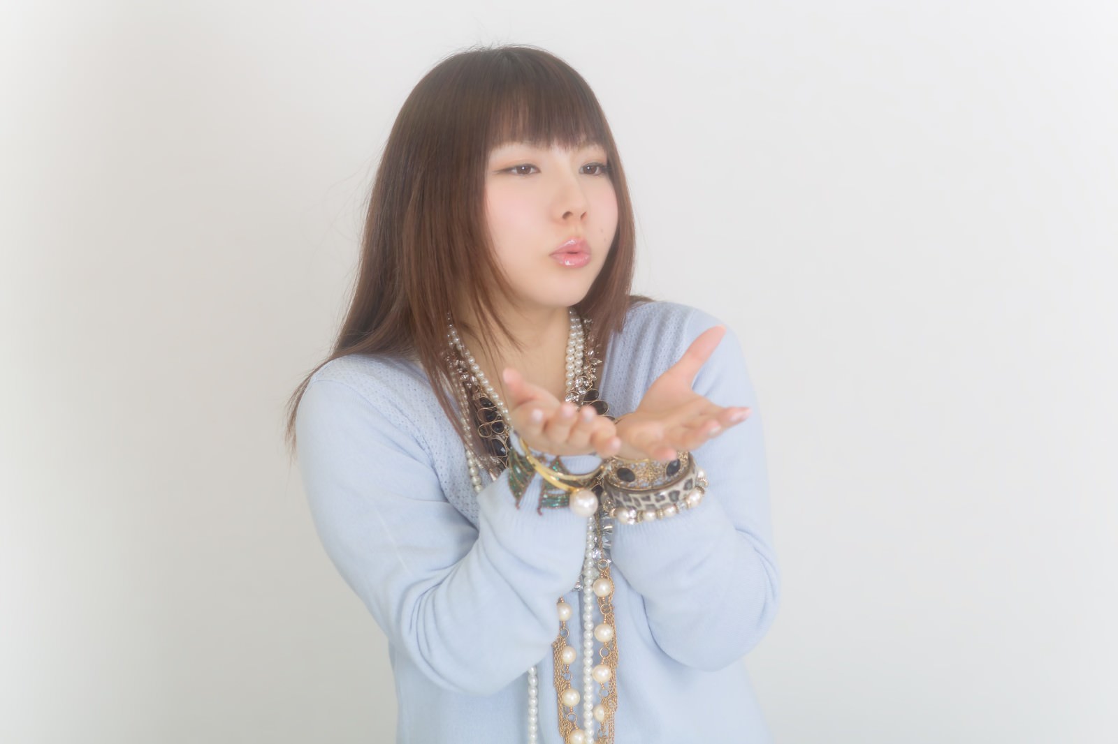 ペール色のシャツにパール調のネックレスを重ねた女性がカメラに向かって微笑む［モデル：Lala］
