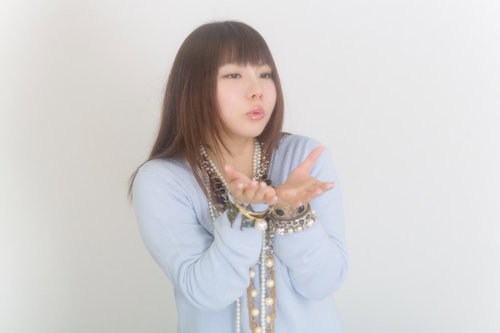 両手を前に出すアクセサリーをつけた水色の服の女性