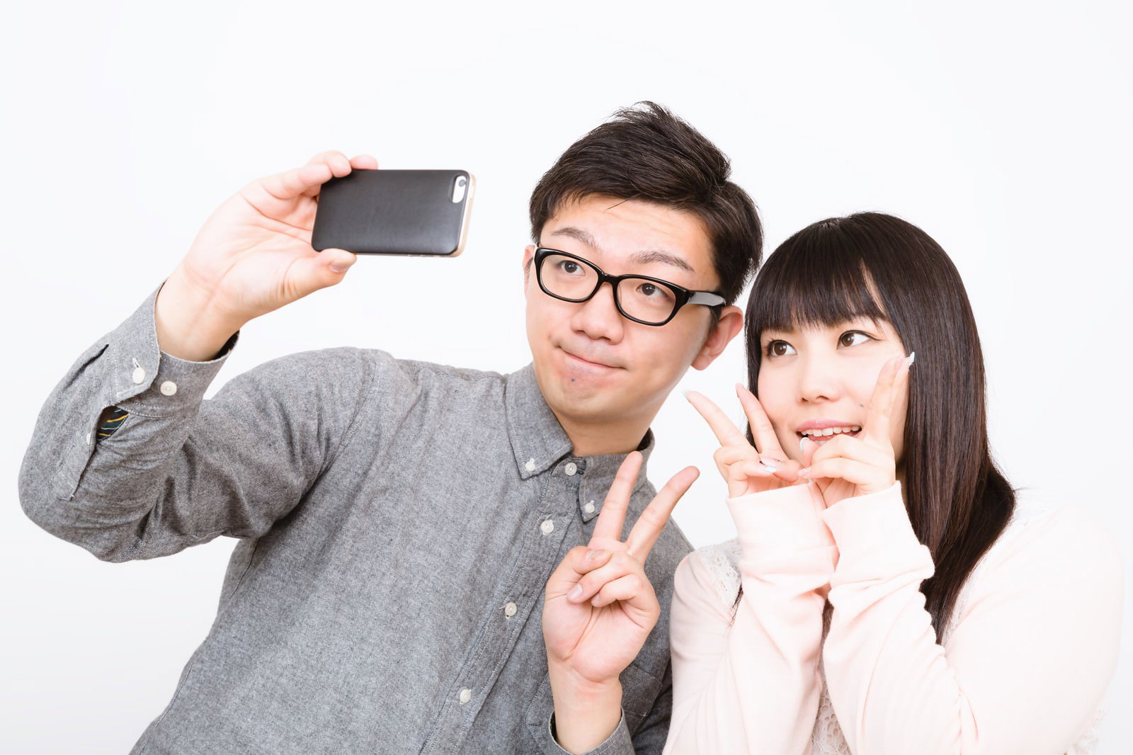 白背景で笑顔でスマホ自撮りする眼鏡の男性と女性［モデル：OZPA Lala］