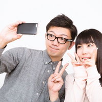 白背景で笑顔でスマホ自撮りする眼鏡の男性と女性の写真