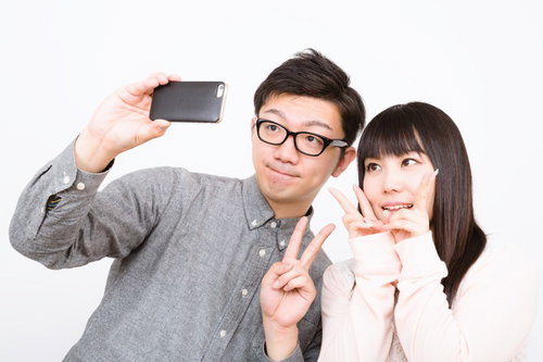 白背景で笑顔でスマホ自撮りする眼鏡の男性と女性