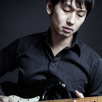 暗いグレー背景で黒い服の男性が白いピックガードの黒いエレキギターを弾くの写真