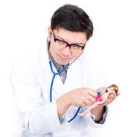 ピンクの豚の置き物に聴診器を当てるお医者さんごっこの男性の写真