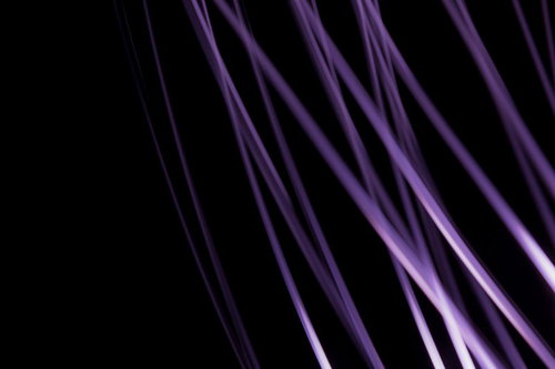 真っ黒な背景に紫色に光る細い線が斜めに流れる抽象写真