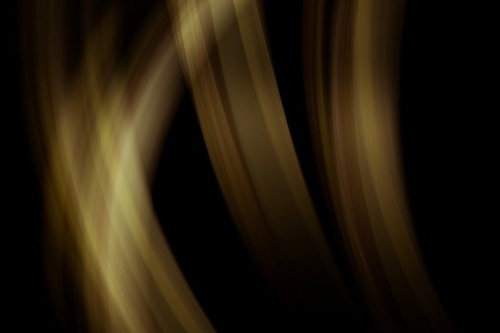 真っ黒な背景に黄色と茶色の帯状の光が曲線を描いて流れる抽象写真