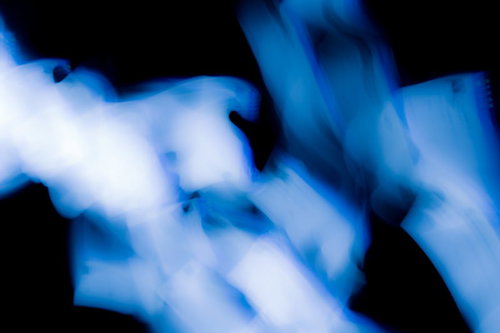 真っ黒な背景に青白く光る煙のような光の筋が横切る抽象写真