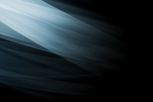 暗い空間で滑らかな布のような素材が波打って流れる抽象写真