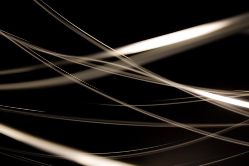 真っ黒な背景に金属の線が斜めに交差して光を反射する抽象写真