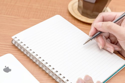 コーヒーとスマートフォンを横にノートに書き込む俯瞰