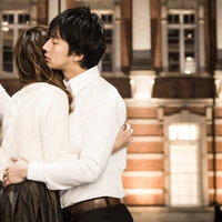 夜間の木造建築前で白いニットとシャツの男女が後ろ姿で抱き合う写真の写真