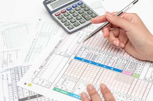 電卓とペンを持って確定申告書を計算する手元