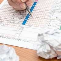電卓を横に確定申告書に記入する手元と丸めた紙の写真