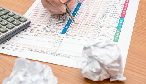 電卓を横に確定申告書に記入する手元と丸めた紙