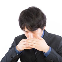 口元を両手で覆う黒ストライプスーツの男性の上半身の写真