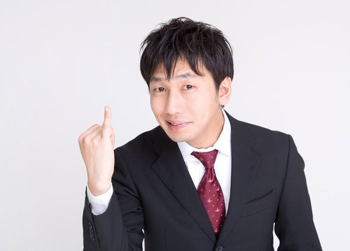 右手の人差し指を立てるスーツの男性