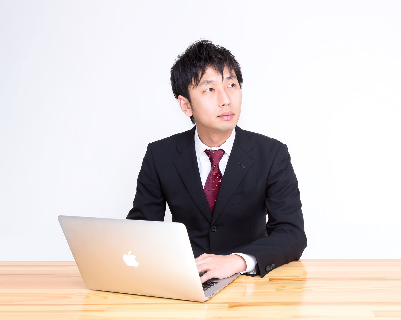 木製デスクでノートPCを操作する黒スーツのサラリーマン［モデル：大川竜弥］