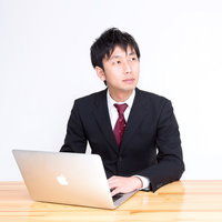 木製デスクでノートPCを操作するスーツのサラリーマンの写真