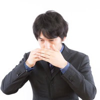 両手で口元を覆うストライプスーツの黒髪の男性の写真