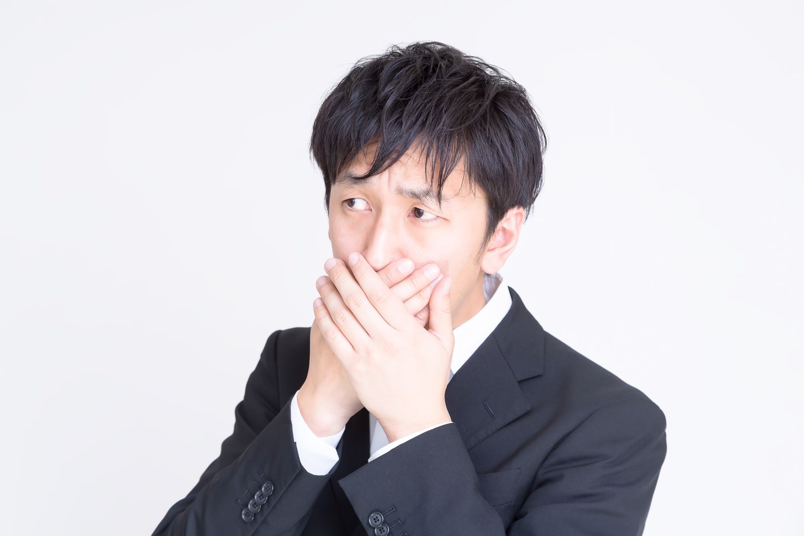 白背景で両手で口元を覆う黒スーツのサラリーマン［モデル：大川竜弥］