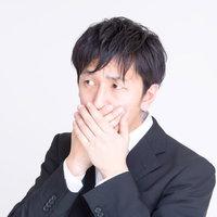 白背景で両手で口元を覆うスーツのサラリーマンの写真