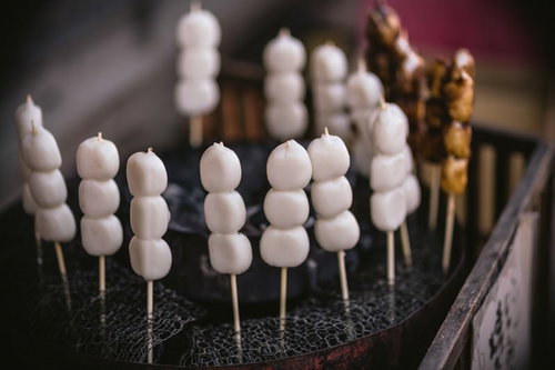 黒い台の上に串に刺さった白い丸い団子が並ぶ接写