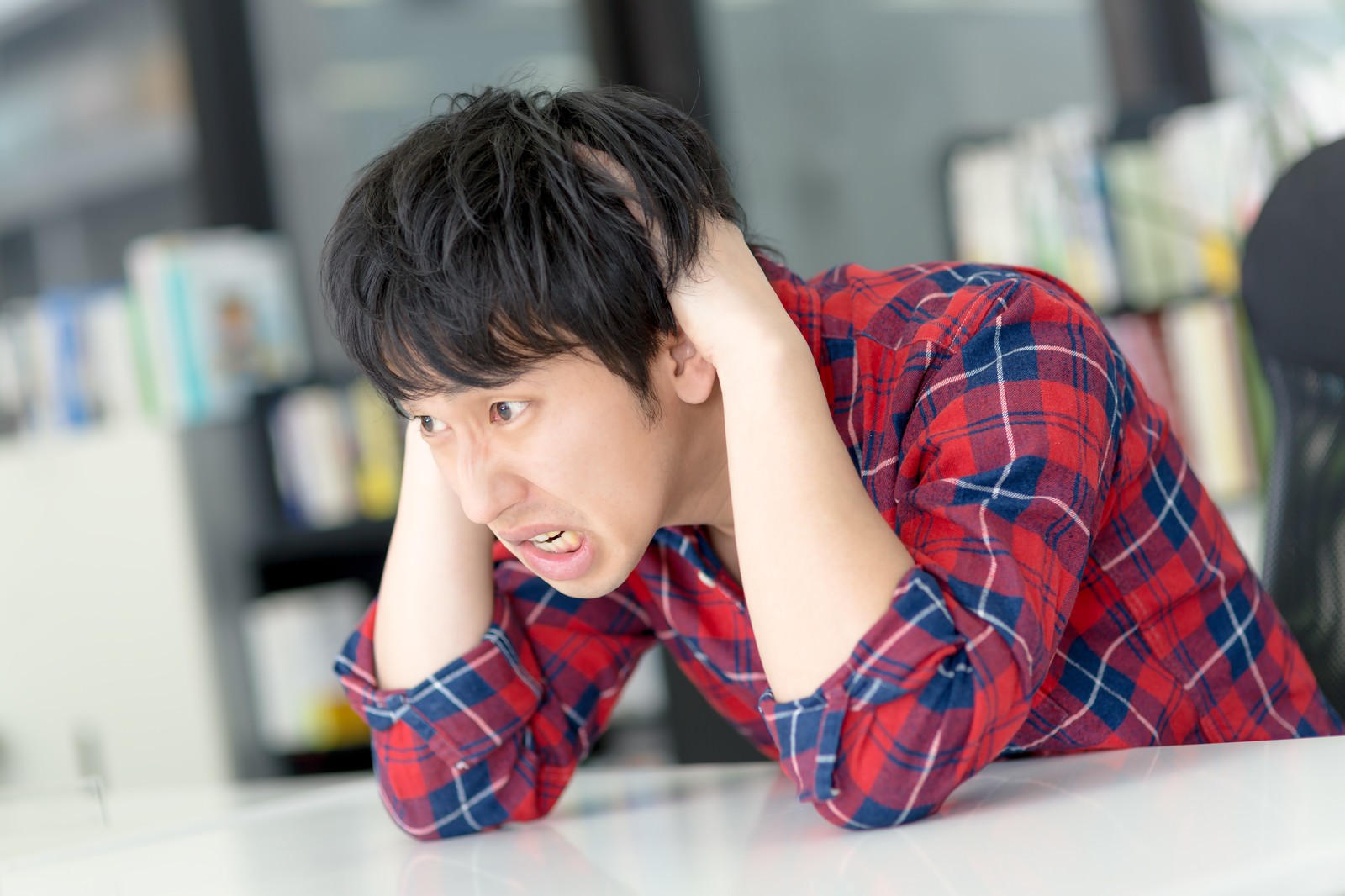 机を叩いて怒る赤いチェックシャツの男性［モデル：大川竜弥］