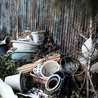 放置された植木鉢やバケツが積み重なったトタン壁の前の写真