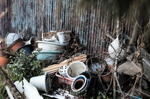 放置された植木鉢やバケツが積み重なったトタン壁の前