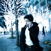 夜の電飾が施された歩道で携帯電話で通話するコートの男性の写真