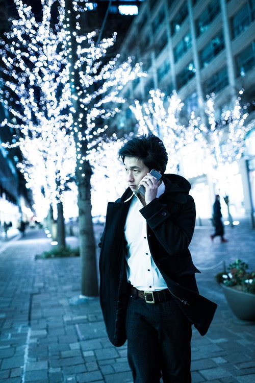 夜の電飾が施された歩道で携帯電話で通話するコートの男性