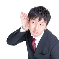 記者の質問に耳を澄ますスーツ姿の男性の写真