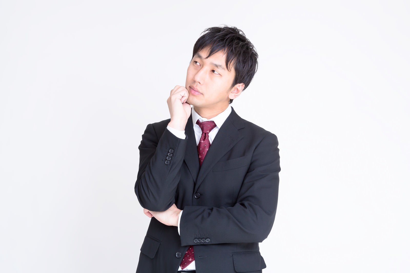 右手を顎に当て左腕を組んで考えるスーツの男性［モデル：大川竜弥］