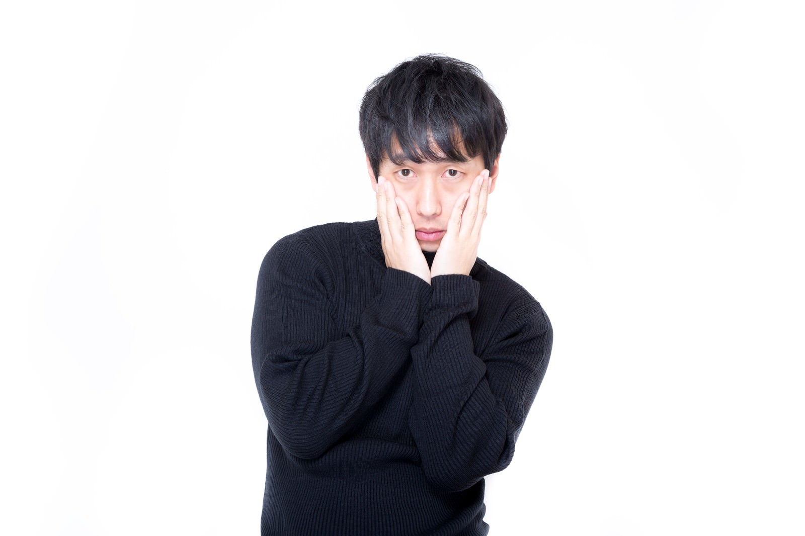 黒いセーターで両手を頬に当てて心配そうな表情の男性［モデル：大川竜弥］