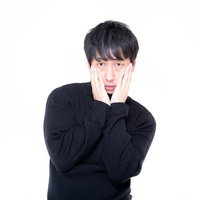 黒いセーターで両手を頬に当てて心配そうな表情の男性の写真