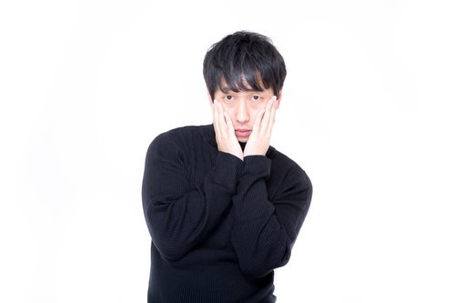黒いセーターで両手を頬に当てて心配そうな表情の男性