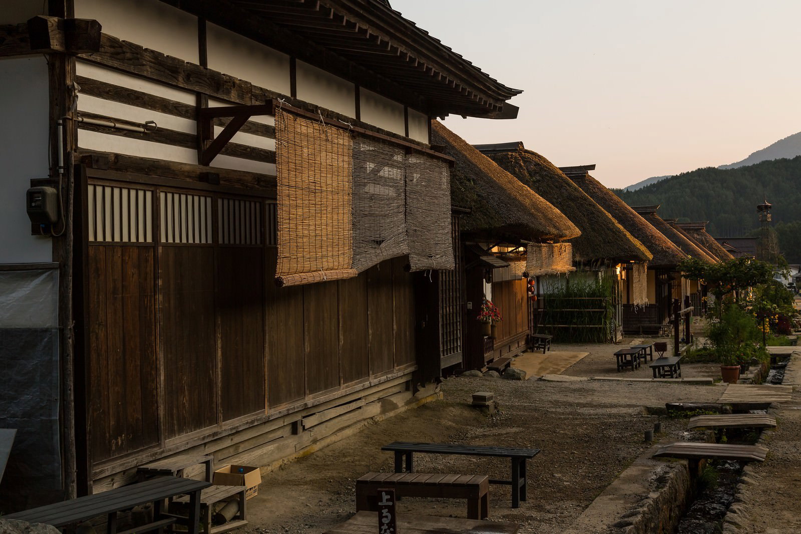 夕暮れの光に照らされた茅葺き屋根の民家が一列に連なる宿場町の街並み