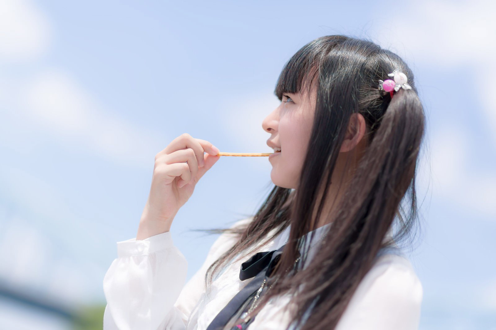 青空の下でお菓子を食べるツインテールの女の子［モデル：こころ］