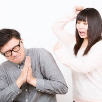 白背景で手を合わせて謝る男性と怒る女性の痴話げんかの写真