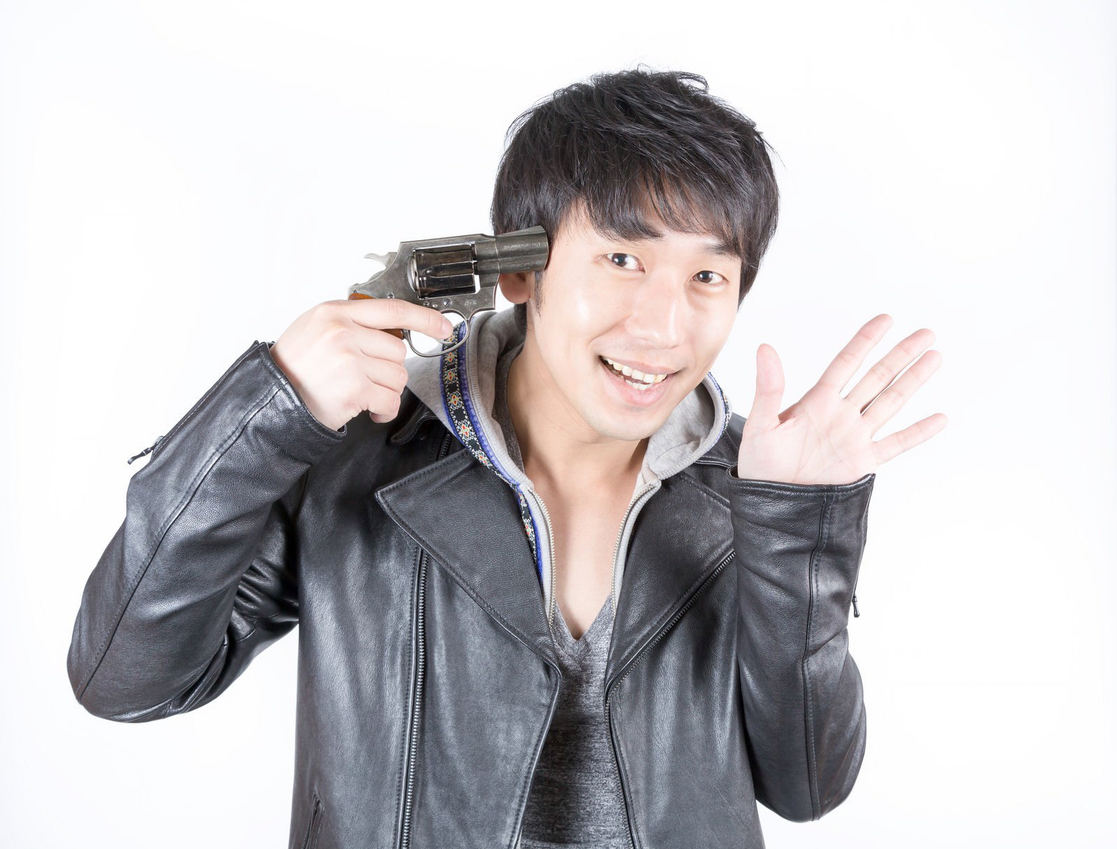 銃を頭に当てて笑顔で左手を挙げる革ジャンの男性［モデル：大川竜弥］