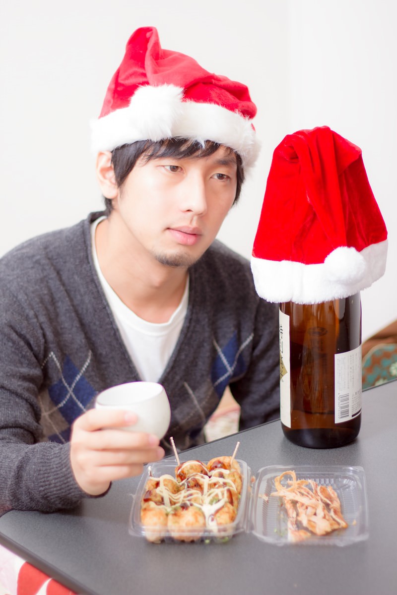 サンタ帽を被ってビールを飲む男性とテーブルの上の酒瓶とつまみ［モデル：大川竜弥］