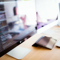 自然光の差すデスクでノートPCに映るコーディング画面の写真