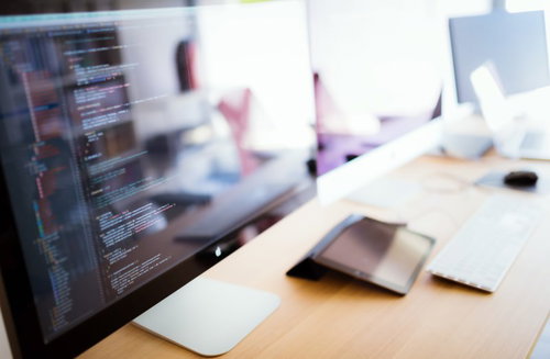 自然光の差すデスクでノートPCに映るコーディング画面