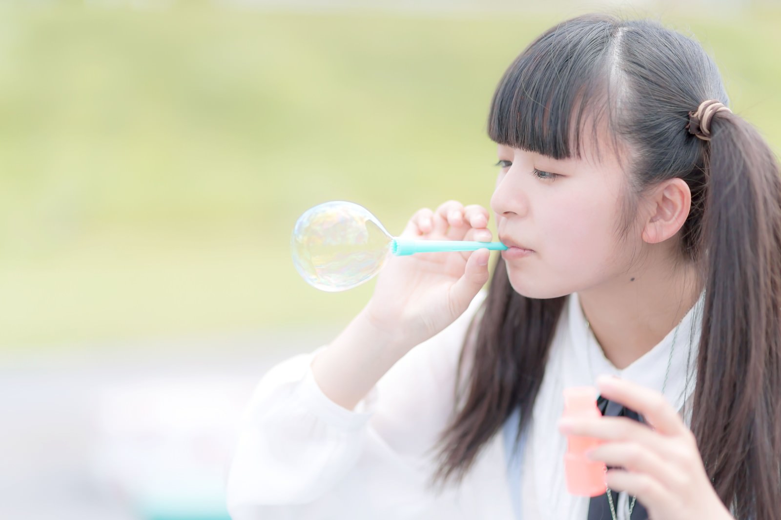 黒髪のツインテールの女の子が水色のシャボン玉吹き器でシャボン玉を吹いている横顔［モデル：こころ］