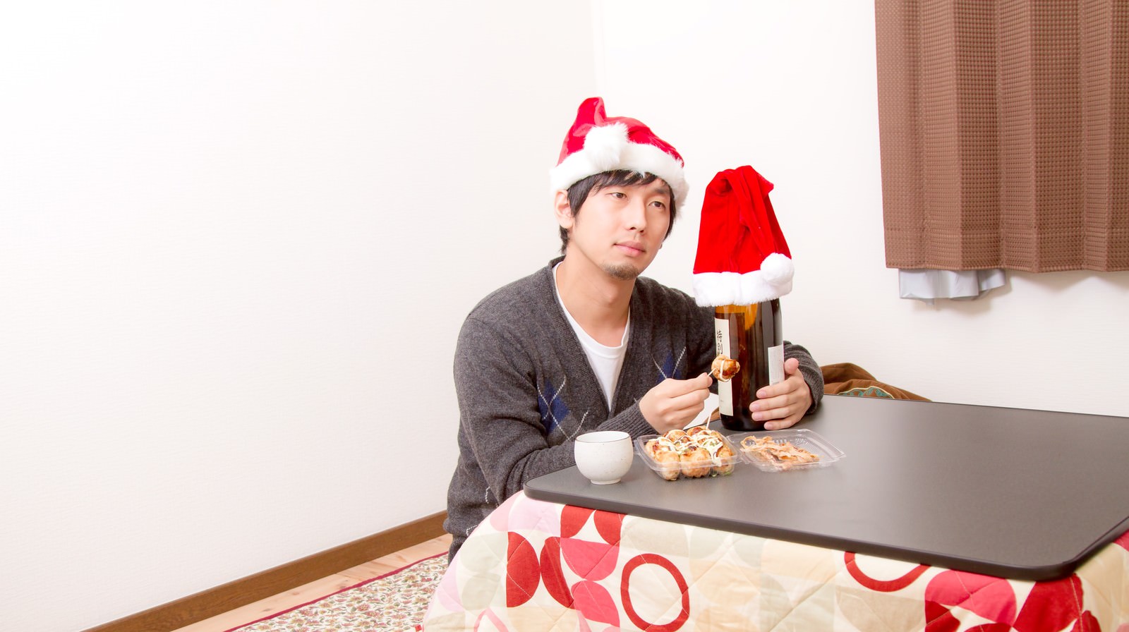 コタツで酒を飲みながらサンタ帽をかぶる男性［モデル：大川竜弥］